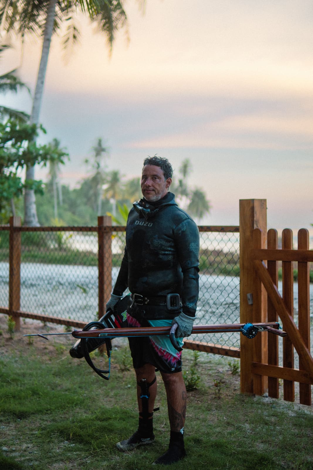 Marcel at the villa gate at dusk, spearfishing gear in hand